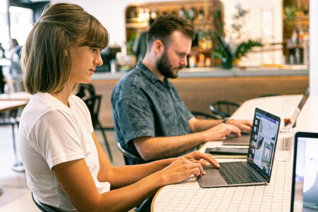  A man and woman sit together at a table, focused on their laptops, indicating a productive work environment.
