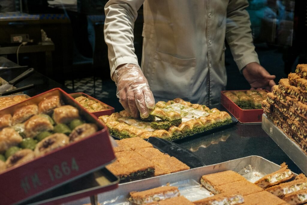  A man carefully arranges food items on trays inside a bustling bakery, preparing for customers.