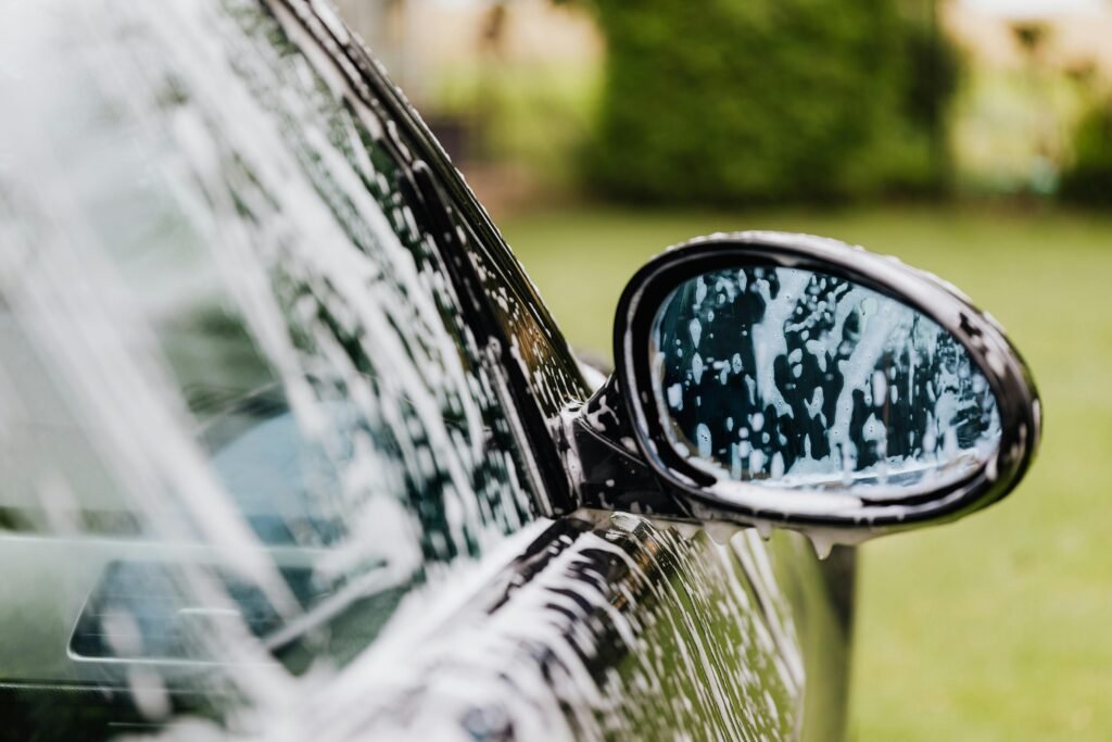 A car is being cleaned with a nozzle at a car wash, showcasing water spraying and soap suds around the vehicle.