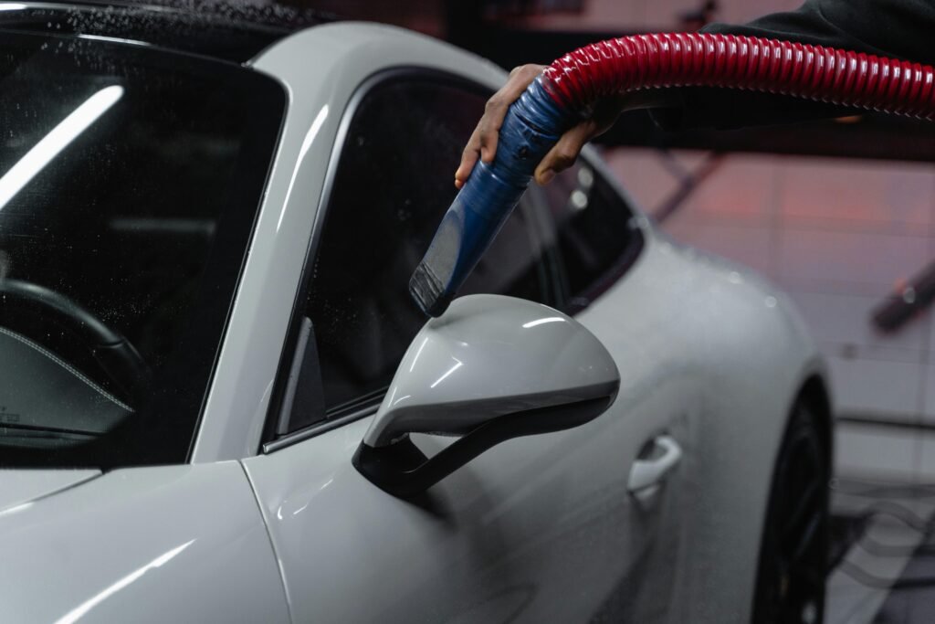  A person cleans a white car using a hose, spraying water to remove dirt and grime from the vehicle's surface.